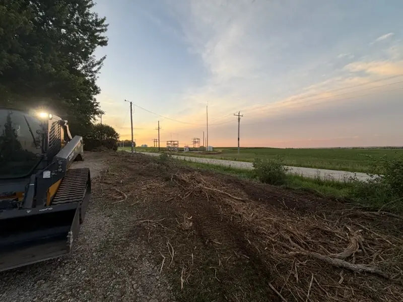 Skid steer beside freshly cleared roadside ground at sunset