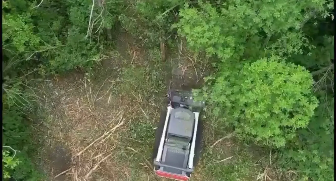 Aerial view of tracked equipment clearing among trees